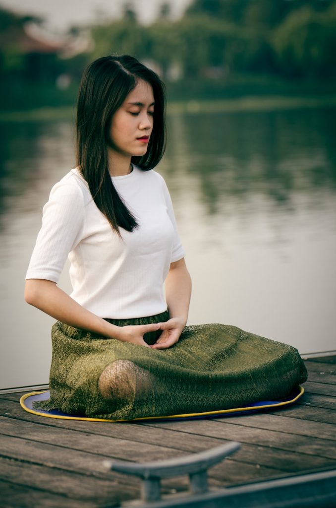 woman meditating on wooden dock during daytime